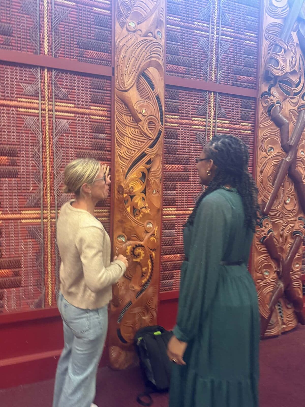 Two people in conversation beside tukutuku panels